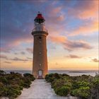 Keine spezifischen Texte. Ein Leuchtturm vor einem malerischen Sonnenuntergang, umgeben von Vegetation und Meer.
