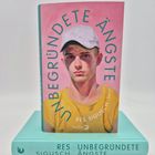 "UNBEGRÜNDETE ÄNGSTE" von Res Sigusch. Cover zeigt einen jungen Mann mit weißer Kappe, gelbem Shirt auf rosa Hintergrund.