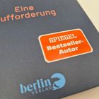 Text: "Eine Aufforderung", "SPIEGEL Bestseller-Autor", "berlin verlag". Oben links ein blauer Bären-Logo.