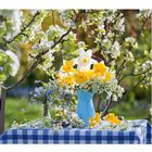 04, daneben ein Kalender. Gelbe und weiße Blumen in blauer Vase auf kariertem Tuch, blühende Zweige im Hintergrund.