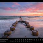"BUHNEN AN DER OSTSEE AUF DEM DARSS, Cornelia & Ramon Dörr. Sandstrand mit Holzpfählen im Meer, Sonnenuntergangshimmel."