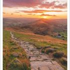 4 | 2027. Ein steiniger Pfad schlängelt sich durch eine hügelige Landschaft bei Sonnenuntergang.