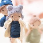 Drei gestrickte Puppen in sanften Farben, mit detaillierten Merkmalen und liebevoll gestalteter Kleidung.