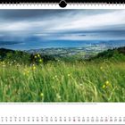 Ein Kalenderblatt für April 2027. Eine grüne Wiese mit gelben Blumen, dahinter eine Stadt am blauen See unter bewölktem Himmel.