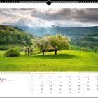 „April“, Frühlingslandschaft mit blühenden Bäumen und grüne Hügel im Hintergrund. Kalenderansicht unten.