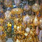 Viele filigrane, goldene Metalllampen hängen dicht gedrängt von der Decke in einem geschäftigen Basar.