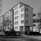 Ein moderner, mehrstöckiger Wohnblock mit Balkonen und großen Fenstern, umgeben von kahlen Bäumen und Gehwegen.