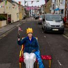 Straßenszene mit einer Person auf einem roten Sessel, golden gekrönt, hält eine kleine Union-Jack-Flagge.