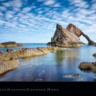 Kalender: März 2027. Motivierend. Felsformation "Bow Fiddle Rock" im Meer, ruhige Wellen und blauer Himmel mit Wolken.