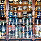 Gestapelte Stoffballen mit Etiketten in einem hölzernen Regal. Zahlreiche Farben und dichtes Muster.