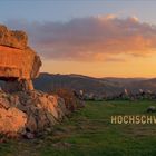 HOCHSCHWARZWALD; Felsformation mit eingravierter Tafel im Vordergrund; Sonnenuntergang über Hügeln im Hintergrund.