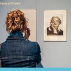 „Traces of Interest“ steht oberhalb. Eine Frau von hinten betrachtet ein Porträt an der Wand.