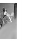 Zwei Personen vor einem Spiegel, eine fotografiert die andere. Schwarz-Weiß-Fotografie mit Pflanzenmuster im Hintergrund.