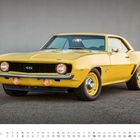 1969er Camaro SS, April. Ein gelbes, sportliches Auto mit runden Scheinwerfern und muskulöser Karosserie steht auf asphaltierter Fläche.