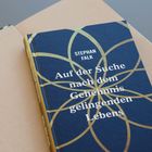 "Stephan Falk, Auf der Suche nach dem Geheimnis gelingenden Lebens." Ein Buch mit blauem Cover und goldenen Mustern.