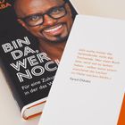 Zitat von Yared Dibaba: Verbindung statt Trennung. Cover zeigt lachenden Mann mit Brille, Titel "Bin da, wer noch?".