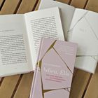 Der Titel des Buches lautet: "Adieu, Ella" von Elke Rutenhofer. Bücher liegen offen auf einem Holztisch.