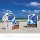 April 2027 | Küstenland Meeresblick. Zwei Strandkörbe am Sandstrand vor blauem Himmel und grünem Meer.