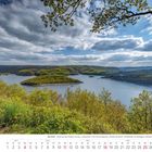 Die Eifel: Blick auf den Rursee und die "Liebesinsel" im April 2027. Waldreiche Landschaft unter blauem Himmel mit Wolken.