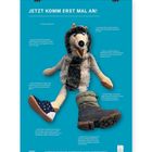 Plakat in Blau mit weißem Text: "JETZT KOMM ERST MAL AN!" Ein Plüschtier-Wolf trägt zwei unterschiedliche Schuhe.