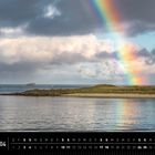 Text: "Lofoten 04". Unten Kalenderdaten. Landschaft mit Regenbogen über grünem Land und Wasser, stürmische Wolken.
