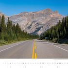 Text: "Der Icefields Parkway (Alberta) zählt zu den landschaftlich reizvollsten Straßen der Welt." 
Blick auf eine Straße, umgeben von Nadelwäldern, Berge im Hintergrund.