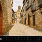 Andalusien 04. Eine malerische, enge Straße mit historischen Gebäuden aus Stein; ein Turm im Hintergrund.