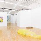 Ein großer, heller Raum mit Holzboden. Links ein Gemälde an der Wand. In der Mitte eine gelbe aufblasbare Struktur.