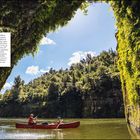 Bootstour auf dem Whanganui River. Zwei Personen in einem roten Kanu paddeln auf einem grün umsäumten Fluss.