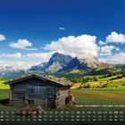 Seiser Alm (Italien) – Hochalm mit Dolomitenblick: Eine Berglandschaft mit grünen Wiesen, Holzhütten und Bergen im Hintergrund.