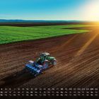 Kalender mit den Tagen und Zahlen. Ein Traktor pflügt ein Feld bei Sonnenaufgang, grüne Felder im Hintergrund.