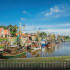 Kalendertext: "Hafen Greetsiel" und Zahlenreihe. Fischerboote im Wasser, traditionelle Häuser im Hintergrund.