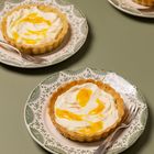 Drei Teller mit grünen Mustern, darauf kleine Törtchen mit Sahne und gelber Soße, je eine Gabel daneben.