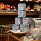 Verkaufspreisschild: "Loraine klein Geschenk 17,50€". Bunte Geschenkboxen in einem Ladenregal.