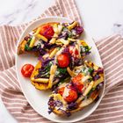 Drei gefüllte Süßkartoffelhälften mit gegrillten Tomaten, Spinat und violettem Kohl, serviert auf einem weißen Teller.