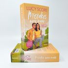 "Buchcover: Lucy Score - Mistakes were made. 'Disaster is her middle name.' Illustration: Paar auf Fahrrad, pastellfarbene Töne."