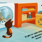 Texte: "Zu Hause ist es nie langweilig." "Es gibt so viele interessante Dinge: die Waschmaschine, die sich immer weiterdreht." Ein Cartoon-Kätzchen betrachtet eine Waschmaschine neben Regalen mit Reinigungsmitteln und einem Wäschekorb.