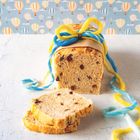 Ein Laib Rosinenbrot, mit gelbem und blauem Garn umwickelt, vor einer Tapete mit bunten Heißluftballons.