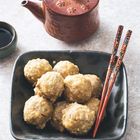 Eine Schale mit mehreren Fleischbällchen, dazu rote Essstäbchen. Daneben eine Teekanne aus braunem Ton.