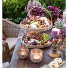 "Oktober. Etagere mit Feigen, Käse und Trauben auf einem Gartentisch. Kerzen und Pflanzen zur Dekoration, gemütliche Atmosphäre."