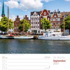 September 2027 Kalenderseite; Segelboote in Lübeck; rechteckige, städtische Gebäude und Bäume im Hintergrund.