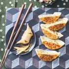 Keine Texte im Bild. Geröstete Teigtaschen auf geometrischem Muster, daneben Stäbchen, Soße und roher Gemüse-Salat.