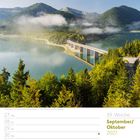 39. Woche, September/Oktober 2027. Tag der Deutschen Einheit. Eine Brücke überquert einen See, umgeben von Bergen und Wald.