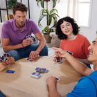 Vier Personen spielen UNO an einem runden Tisch, lachen und genießen das Spiel.