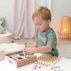 Ein Kind spielt mit einem Montessori-Lernspielzeug und sortiert bunte Kugeln. Im Hintergrund gemütliche Einrichtung.