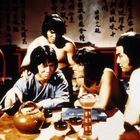 Chinesische Schriftzeichen im Hintergrund. Fünf Männer, teils mit nacktem Oberkörper, sitzen um einen Tisch mit Keramikgefäß.