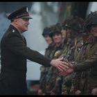 Ein militärischer Offizier in Uniform schüttelt einer Gruppe von Soldaten in Tarnkleidung die Hand. Alle wirken freundlich.