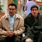 Zwei Männer sitzen in einem Wartebereich. Der ältere trägt eine beige Jacke, der jüngere ist in eine Decke eingewickelt.