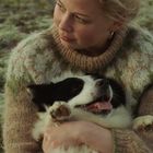 Keine Texte vorhanden. Eine Frau hält einen schwarz-weißen Hund im Arm und blickt liebevoll zur Seite. Sie trägt einen gestrickten Pullover.