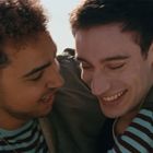 Zwei lachende Menschen umarmen sich herzlich, tragen gestreifte Oberteile. Sie sind eng beieinander und scheinen glücklich.